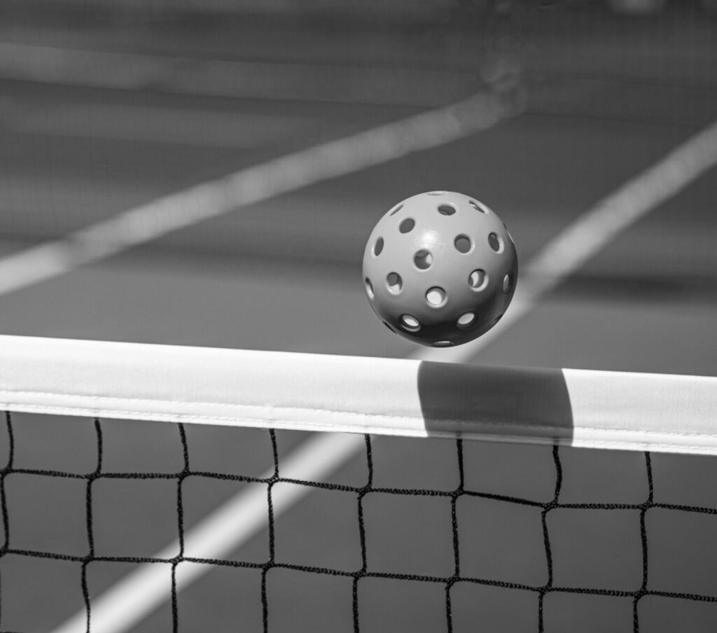 Orange Pickleball crossing a Pickleball net with shadow on the top tape.